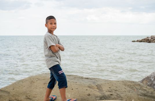 Portrait of a boy standing on a rock with a sea background.