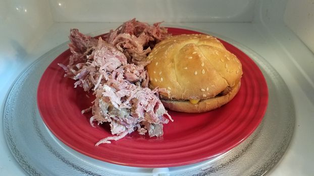 hamburger with bun and pulled pork on red plate in microwave