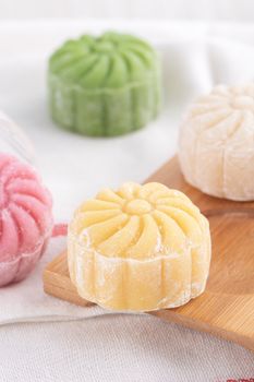 Colorful snow skin moon cake, sweet snowy mooncake, traditional savory dessert for Mid-Autumn Festival on bright wooden background, close up, lifestyle.