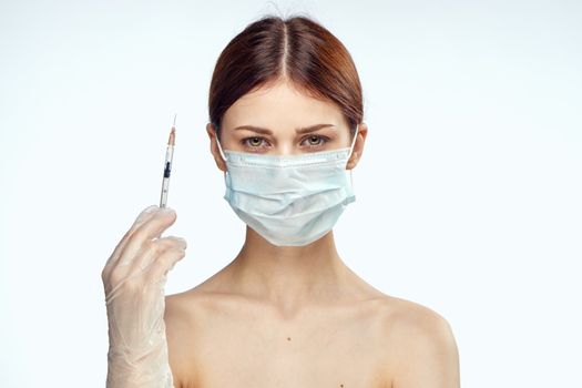 woman holding syringes in her hand injections medical mask naked shoulders rejuvenation light background. High quality photo