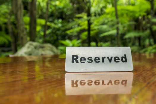 Reserved sign made out stainless steel plate on a laminated wooden table of a restaurant with trees and forest in the background.