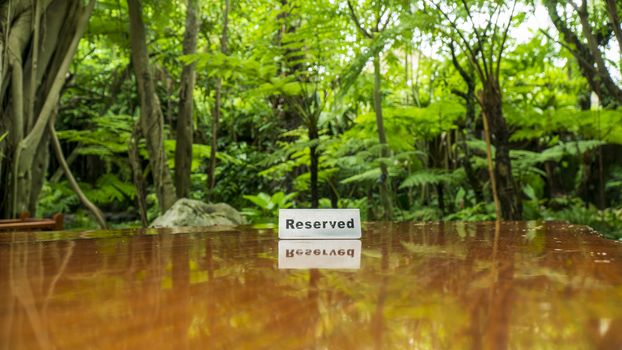 Reserved sign made out stainless steel plate on a laminated wooden table of a restaurant with trees and forest in the background.