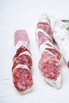 Variety of dry cured fuet and chorizosalami sausages, whole and sliced on white textured background.