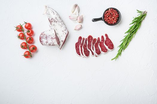Sliced cuts of longaniza, dry cured spanish sausage with herbs and spices on white surface, flat lay with copy space.