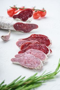 Sliced cuts of longaniza, dry cured spanish sausage with herbs and spices on white textured background.