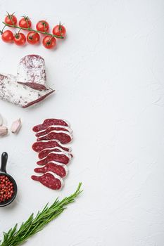 Sliced cuts of longaniza, dry cured spanish sausage with herbs and spices on white surface, top view with copy space.