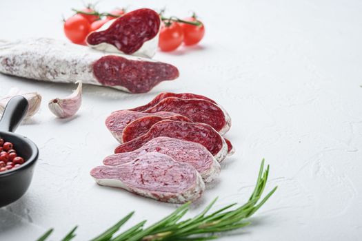 Sliced cuts of longaniza, dry cured spanish sausage with herbs and spices on white surface with copy space.