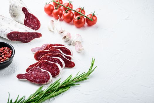 Sliced cuts of longaniza, dry cured spanish sausage with herbs and spices on white textured background with space for text.