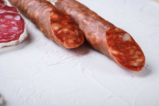 Variety of dry cured fuet and chorizosalami sausages, whole and sliced on white textured background with space for text.