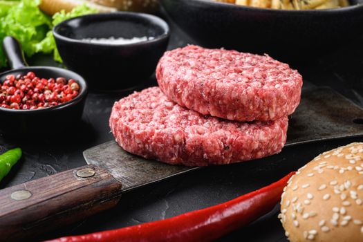 Raw ground beef cutlets with ingredients for burger on black background.