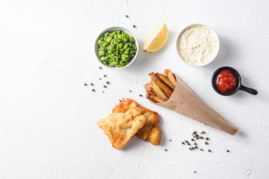 Fried fish and chips in a paper cone on white background with all components classic recipe takeaway food top view white stone textured background space for text.