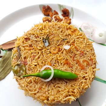 Colorful Delicious yummy prawn briyani with prawn fry in center with prawn fry and raita plated beautifully in white plate with bayleaf and it's one of favorite restaurant cuisine food