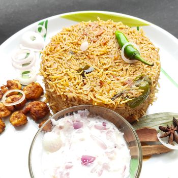 Colorful Delicious yummy prawn briyani with prawn fry in center with prawn fry and raita plated beautifully in white plate with bayleaf and it's one of favorite restaurant cuisine food