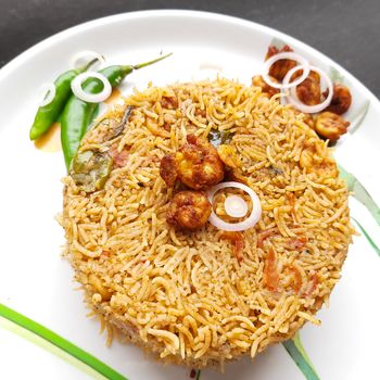 Colorful Delicious yummy prawn briyani with prawn fry in center with prawn fry and raita plated beautifully in white plate with bayleaf and it's one of favorite restaurant cuisine food