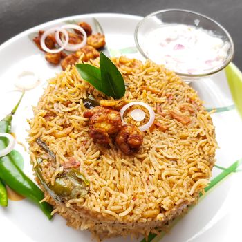 Colorful Delicious yummy prawn briyani with prawn fry in center with prawn fry and raita plated beautifully in white plate with bayleaf and it's one of favorite restaurant cuisine food