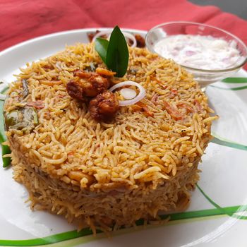 Colorful Delicious yummy prawn briyani with prawn fry in center with prawn fry and raita plated beautifully in white plate with bayleaf and it's one of favorite restaurant cuisine food