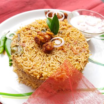 Colorful Delicious yummy prawn briyani with prawn fry in center with prawn fry and raita plated beautifully in white plate with bayleaf and it's one of favorite restaurant cuisine food