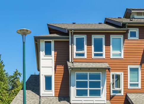 Corner of new townhouse unit with street light pole in front on blue sky background