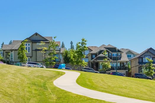 Paved pathway over green lawn on the slope in front of new townhouses Residential town homes on sunny day with blue sky background