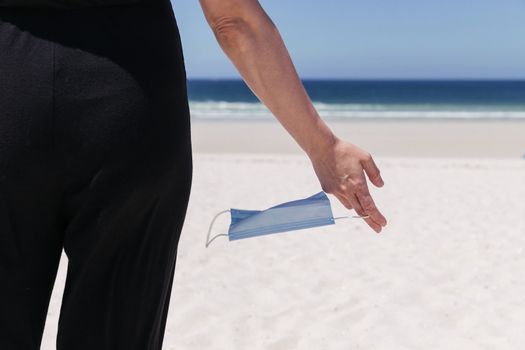 Female hand holding a wind-swept medical mask with the sea in the background