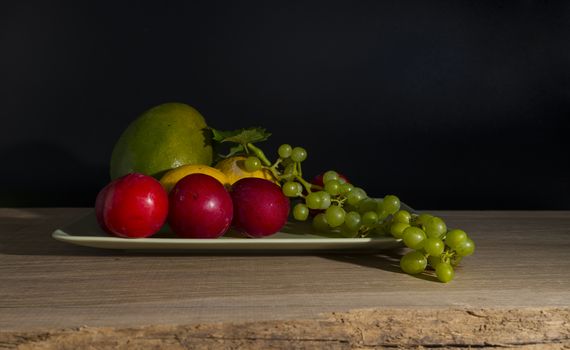 still life with a green bowl on a reflective background with mango,lemons,grapes and plums