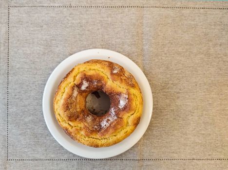 Circular cornmeal cake on a white plate, seen from above, on a gray towel.