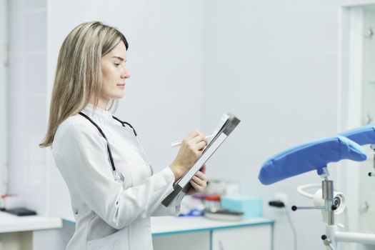A female doctor or nurse in uniform, making notes on the medical form of the patient's medical history. Located in the gynecology office. Stethoscope phonendoscope on the neck