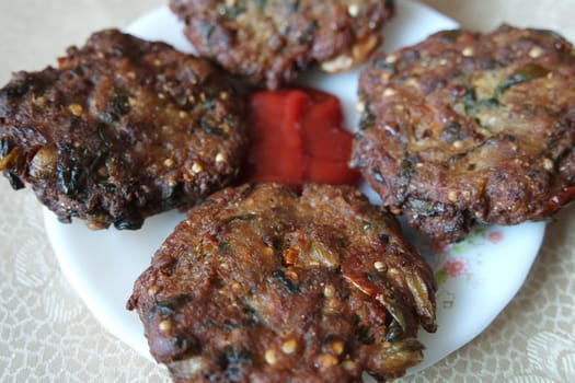Delicious spicy fried round kebab served in white ceramic plate on a wooden floor with red sauce.