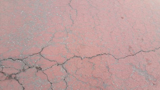 Red colored damaged road or paved pathway with crackes of different shpaes. Cracked texture with copy space for text and messages