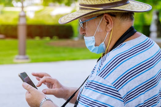 Portrait of old man a wearing medical mask with using smartphone while listening protect during coronavirus COVID-19 in a park