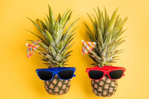 Celebrate Summer Pineapple Day Concept, Top view flat lay of funny two pineapples in sunglasses, studio shot isolated on yellow background, Holiday summertime in tropical