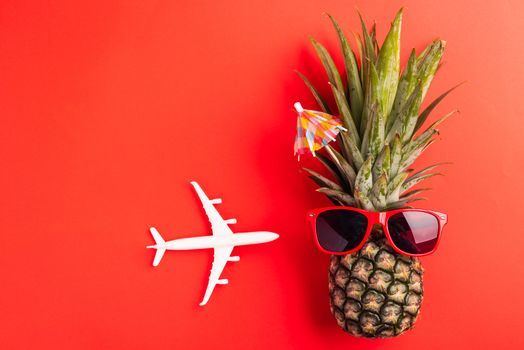 Celebrate Summer Pineapple Day Concept, Top view flat lay of funny fresh pineapple wear red sunglasses with model plane, isolated on red background, Holiday summertime in tropical