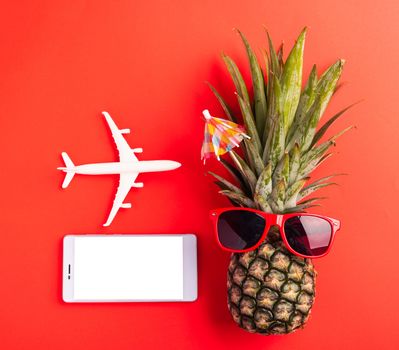 Celebrate Summer Pineapple Day Concept, Top view flat lay of funny pineapple wear red sunglasses, model plane, and smartphone blank screen, isolated on red background, Holiday summertime in tropical