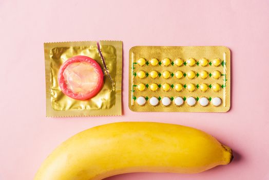 World sexual health or Aids day, Top view flat lay condom on wrapper pack, banana and contraceptive pill, studio shot isolated on a pink background, Safe sex and reproductive health concept