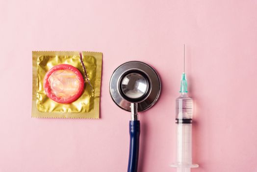 World sexual health or Aids day, Top view flat lay medical equipment, condom in pack and stethoscope, studio shot isolated on a pink background, Safe sex and reproductive health concept