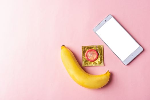 World sexual health or Aids day, Top view flat lay condom in wrapper pack and smart mobile phone blank screen, studio shot isolated on a pink background, watching porn content on mobile phone concept