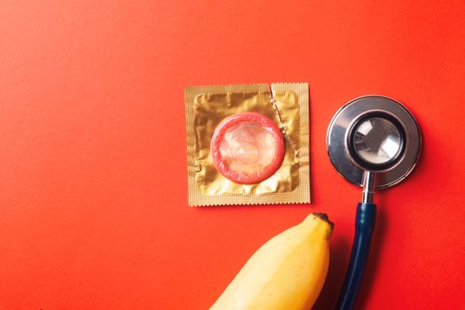 World sexual health or Aids day, Top view flat lay condom in wrapper pack, banana and doctor stethoscope, studio shot isolated on a red background, Safe sex and reproductive health concept