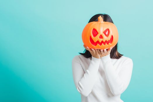 Portrait of Asian beautiful young woman holding orange model pumpkins at her head, funny happy female with ghost pumpkins, studio shot isolated on blue background