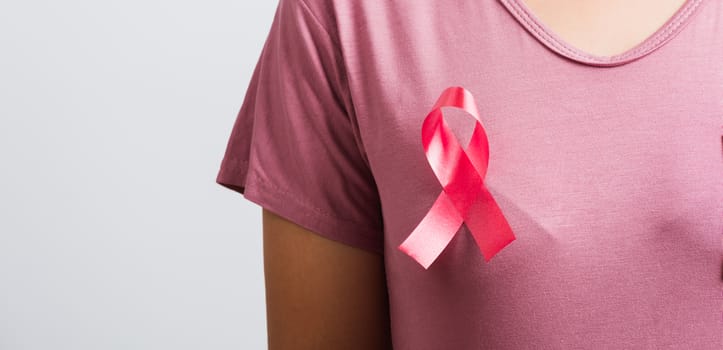 Breast cancer awareness healthcare and medicine concept. Close up Asian woman wear pink shirt standing with pink breast cancer awareness ribbon pin on chest, studio shot isolated on white background