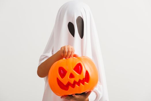 Funny Halloween Kid Concept, little cute child with white dressed costume halloween ghost scary he holding orange pumpkin ghost on hand, studio shot isolated on white background