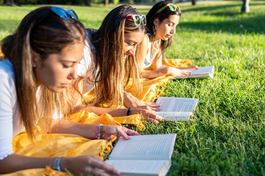 University female students lying on the grass at the park in the morning reading a paperback book - Relaxing outdoor sharing your passion - Return to old healthy habits - Loving nature