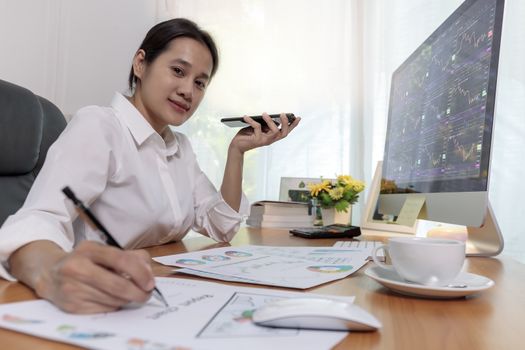 Business women holding smart phone to speak with speaker phone and taking write notes on desk at office. Business people call for working with customer or partner with smart phone. Business concept.
