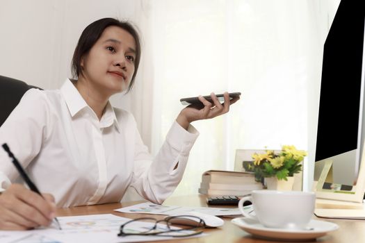 Business women holding smart phone to speak with speaker phone and taking write notes on desk at office. Business people call for working with customer or partner with smart phone. Business concept.