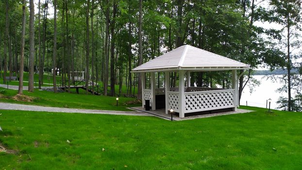 White gazebo in forest with trimmed lawn.