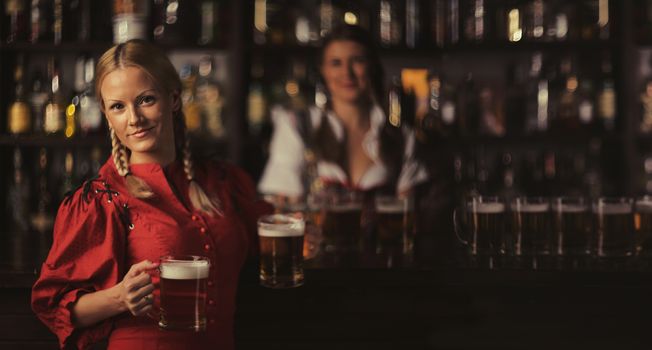 Pretty oktoberfest blonde woman holding beer mugs in bar