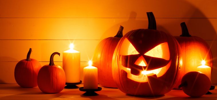 Halloween pumpkin head lanterns and burning candles on wooden background