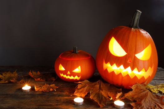 Halloween pumpkin head lanterns burning candles and dry maple leaves on wooden background