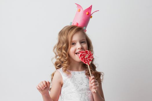 Beautiful little candy princess girl in crown lick big pink heart lollipop