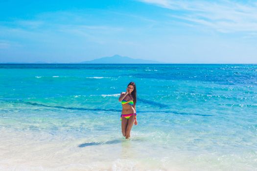 Pretty smiling girl in bikini standing in transparent water of tropical sea