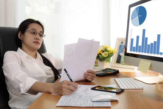 Business woman working in office with computer holding chart report paper and looking. business people working at home with paper and PC screen. Business and finance ,work at home concept